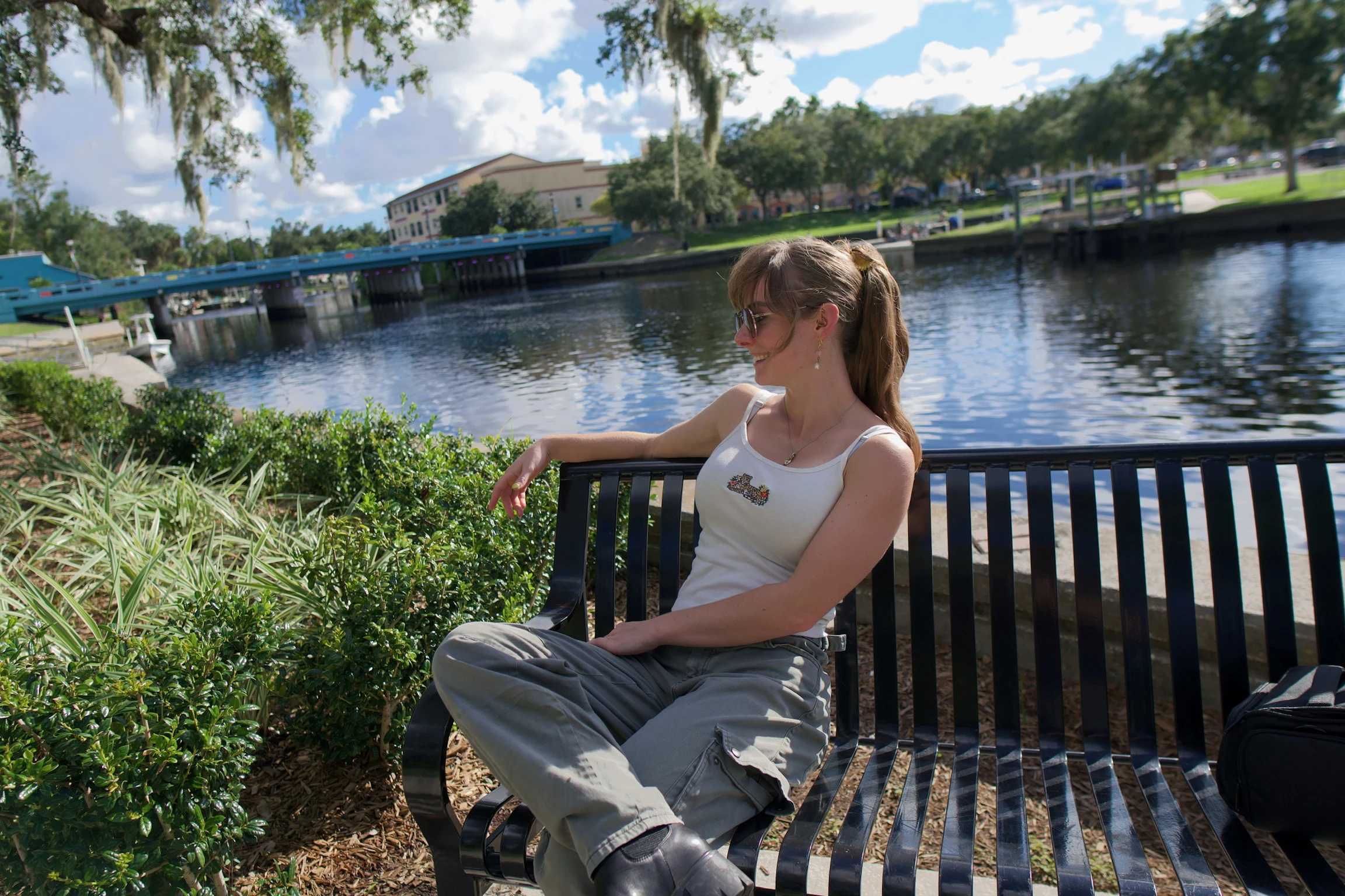 A woman on a black metal bench by the water, looking down